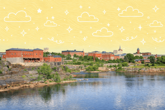 Scenic view of Lewiston, Maine's riverside with historic brick buildings and blue sky.