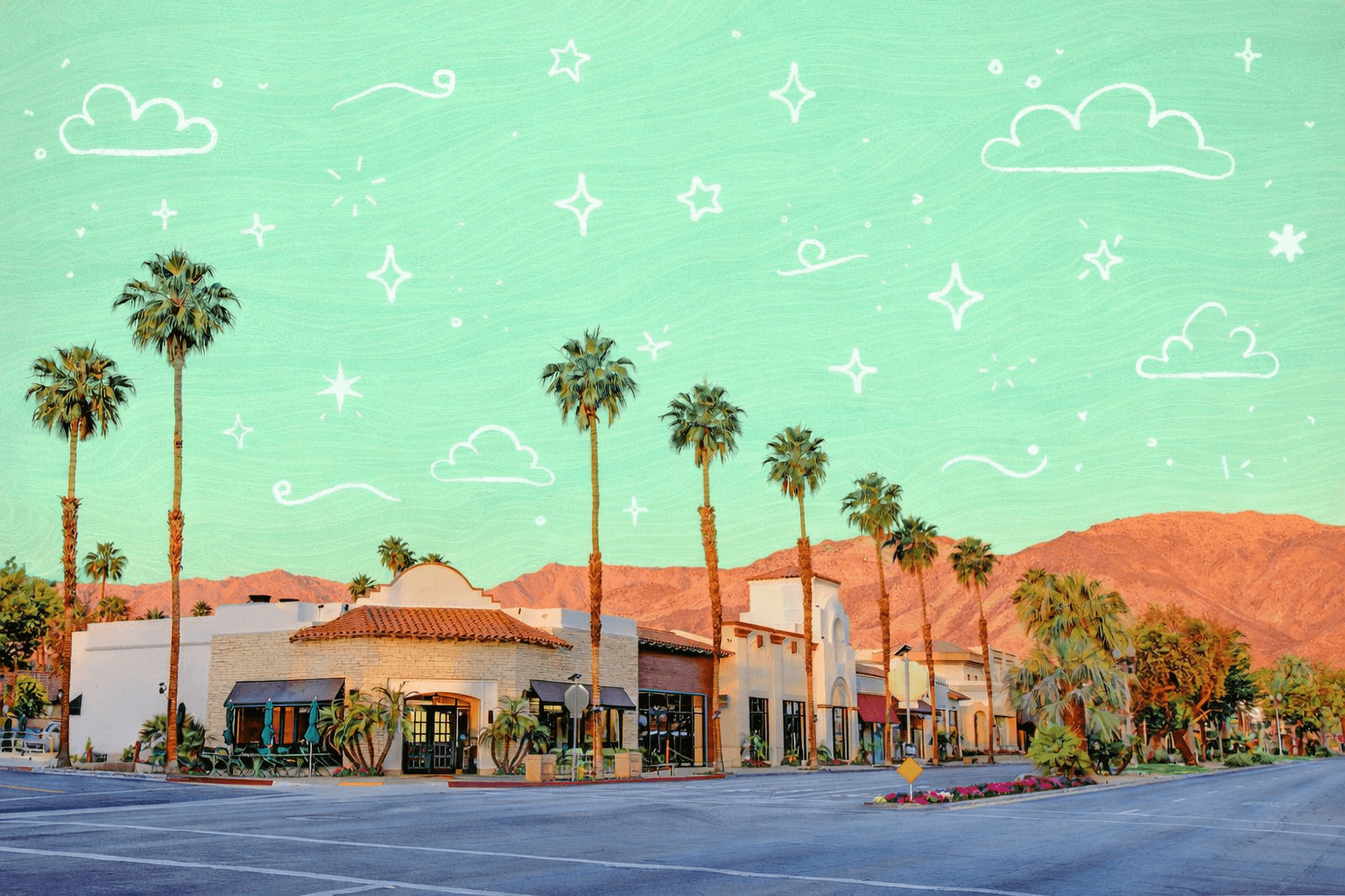 Palm lined street with Spanish style buildings and mountain backdrop at sunset in Palm Desert, California