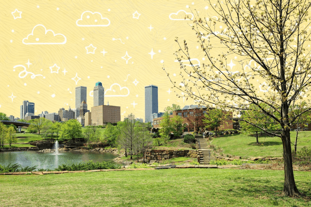 View of Tulsa, OK skyline from a park with a pond and trees in the foreground on a sunny day.